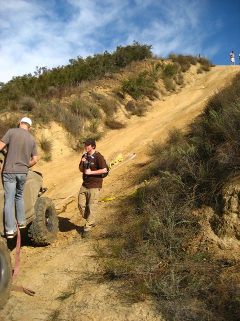 1989 Ford Bronco - Off-road vehicles and people on a steep sandy hill with brush and blue sky.