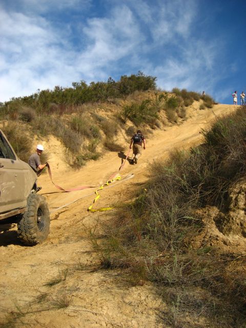 1989 Ford Bronco - An off-road SUV is positioned on a steep dirt incline with a tow strap connected.