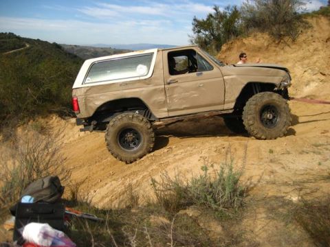 1989 Ford Bronco - This 1989 Ford Bronco is shown off-roading on a dusty, hilly terrain with a clear blue sky overhead.