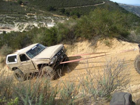 1989 Ford Bronco - Ford Bronco is being towed up a steep dirt hill with tow straps attached to the front.