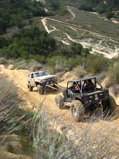 1989 Ford Bronco - Two off-road vehicles navigate a steep, dusty trail with one vehicle assisting the other.