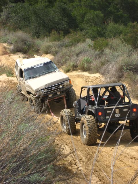 1989 Ford Bronco - Two off-road vehicles navigate a challenging dirt trail, with one vehicle assisting the other.