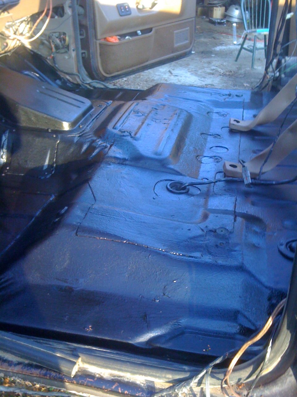Freshly coated dark blue floor pan inside a stripped SUV cab with seat belts and open door