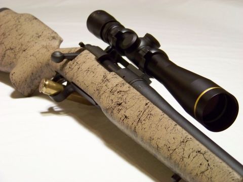 1995 Mercury Grand Marquis - A close-up view of a rifle's action, scope, and stock, with a single cartridge visible.