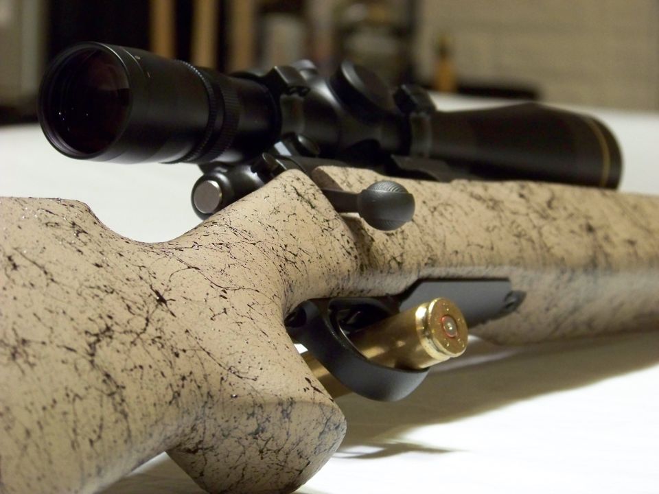 Rifle with scope and a brass cartridge in the ejection port, tan speckled stock