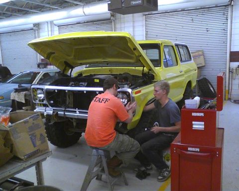 1978 Ford Bronco - Two people work on the front end of a yellow 1978 Ford Bronco in a garage setting.