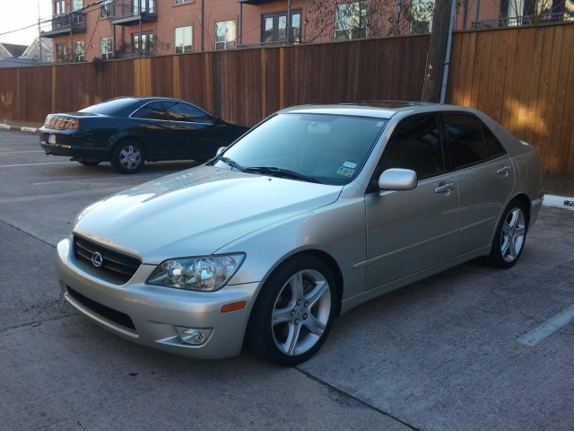 Silver sedan parked in a lot, front 3/4 view. Tinted windows, alloy wheels, visible front grille and headlights