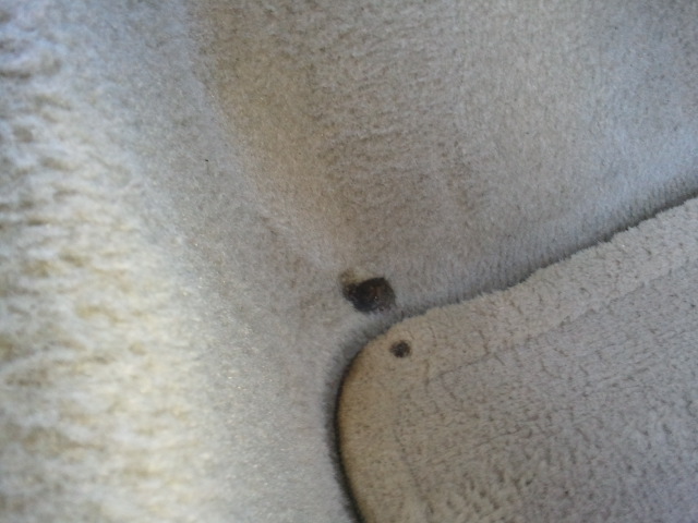 Car interior carpet with dark stains and a small hole