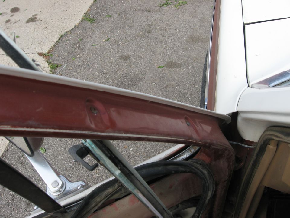 Close-up of a car's door frame, showing the red painted metal and window seal. Part of the white exterior is visible