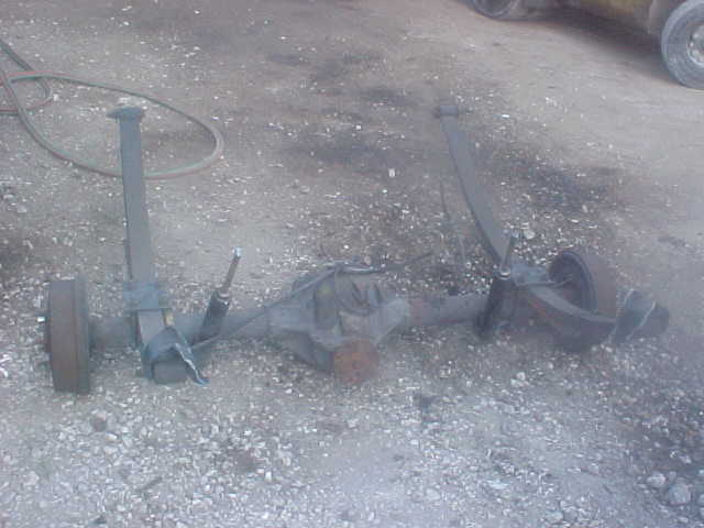 Rear axle assembly with leaf springs and drum brakes, lying on gravel
