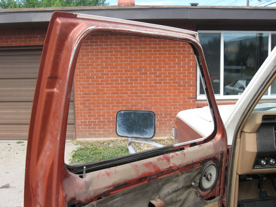 Orange car door frame with a wing window opening. A side mirror is visible. The interior dashboard and a speaker are also seen