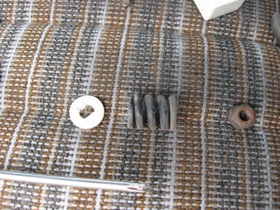 White washer, four rubber grommets, and a nut on a striped fabric surface. A screwdriver is also visible