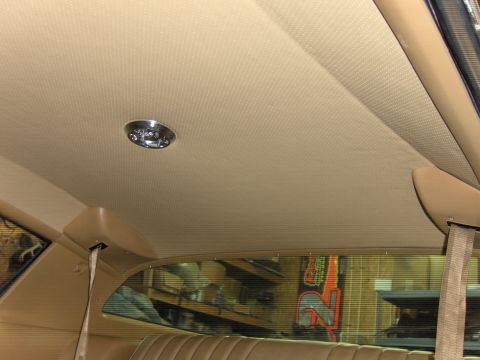 1982 Chevrolet Camaro - Close-up of the interior ceiling light and a tan seatbelt, with a view through the window of a workshop.