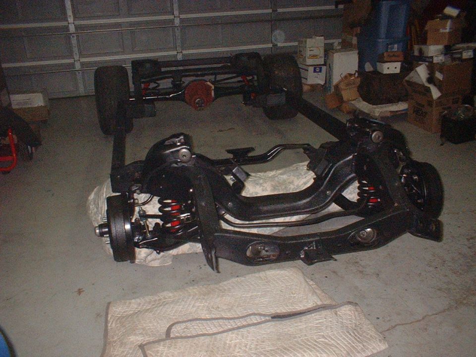 Car chassis and suspension components laid out on the floor