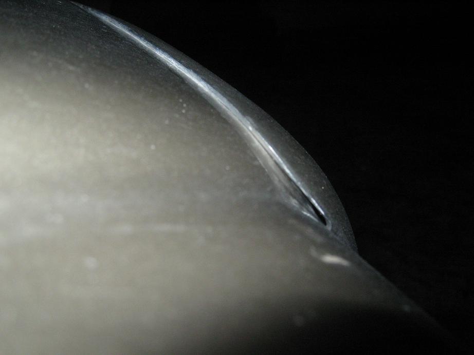 Close-up of a silver car body panel with a sharp crease and a small opening, against a black background