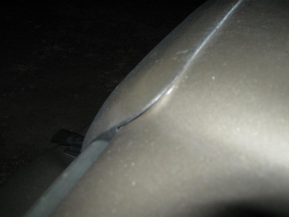 Close-up of a car's beige fender and gray trim piece. Watermark reads SUPERMOTORS.NET