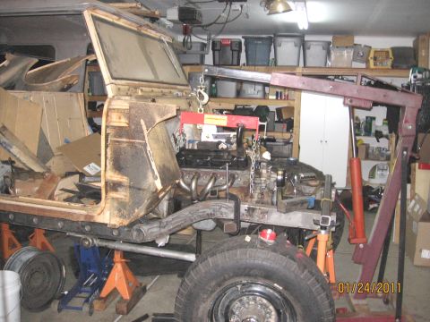 1961 International Scout 800 - The engine is being lowered into the chassis of a vehicle, likely undergoing a motor install or transmission work.