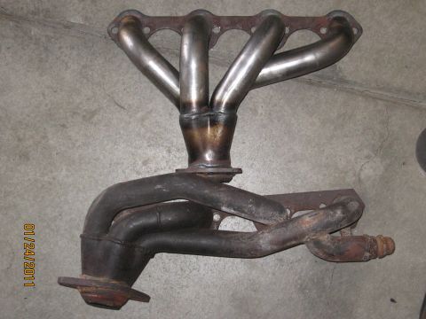 1961 International Scout 800 - Exhaust manifold with four pipes merging into one collector, resting on a concrete surface.