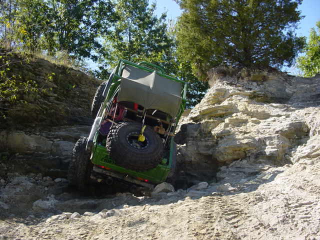 Green off-road vehicle with a roll cage and large tires navigating a rocky incline