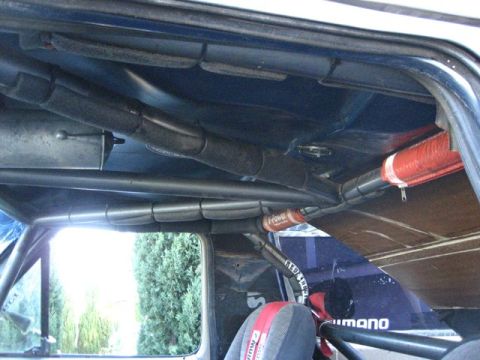 1989 Ford Bronco - The interior of a vehicle shows a complex roll cage structure and a racing seat with a red harness.
