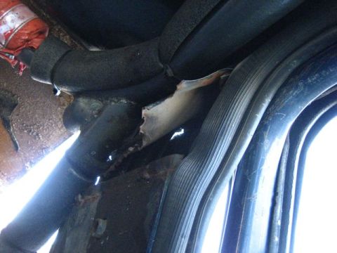 1989 Ford Bronco - Close-up view of the undercarriage of a vehicle, showing damaged metal and hoses.