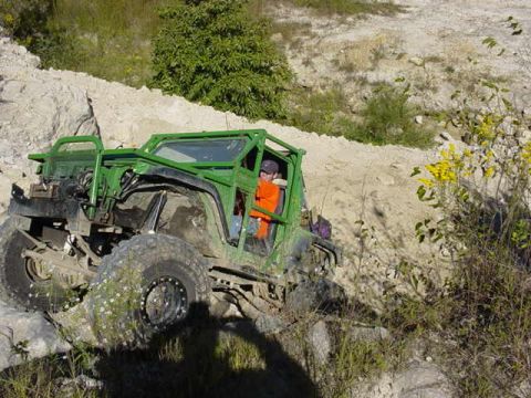1992 Ford Bronco - A heavily modified green off-road vehicle tackles a challenging rocky trail.