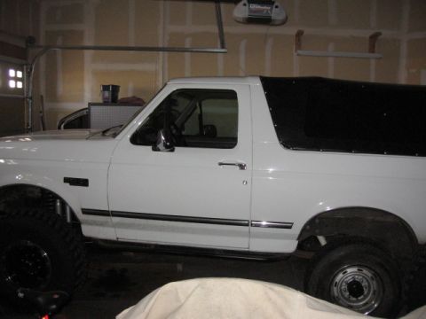 1995 Ford Bronco - Side view of a white SUV with a black soft top, parked indoors.