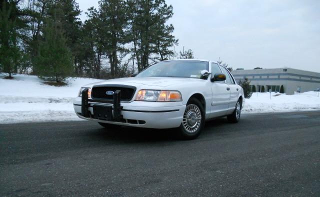 White Ford Crown Victoria with a push bar, parked on asphalt with snow in the background