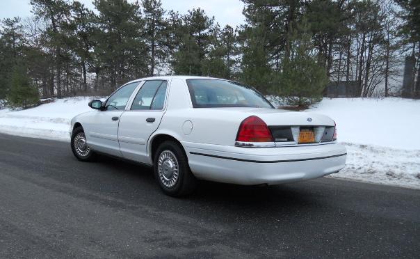 White sedan parked on a wet road with snow on the side, rear view