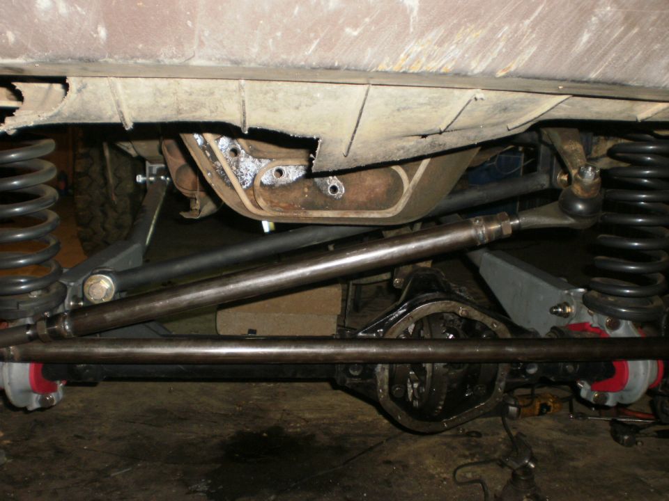 Underbody view of a lifted solid front axle with coil springs and steel tie rod