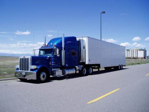 2009 Kenworth T800 - A blue semi-truck with a white trailer is parked on the side of a road under a blue sky with scattered clouds.