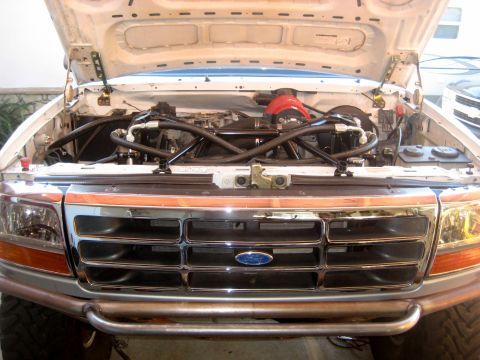 1996 Ford Bronco - Head-on view of a white Ford truck in a garage with the hood raised, showing the chrome grille with blue Ford oval, amber-corner headlights…
