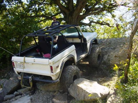 1992 Ford Bronco - This white off-road SUV navigates a rocky terrain, a prominent roll cage and large tires.