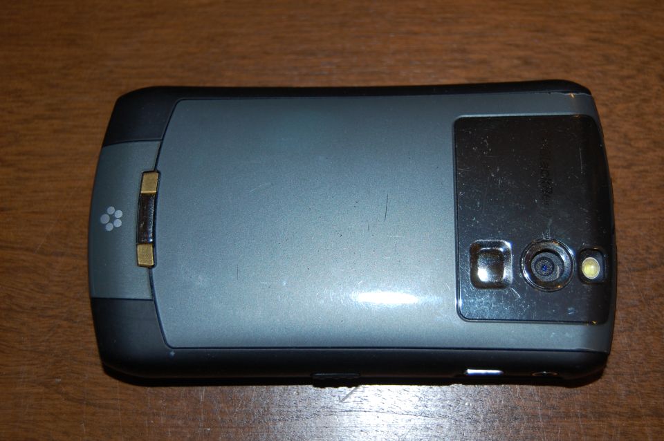 Back of a gray and black cell phone with a camera lens and flash