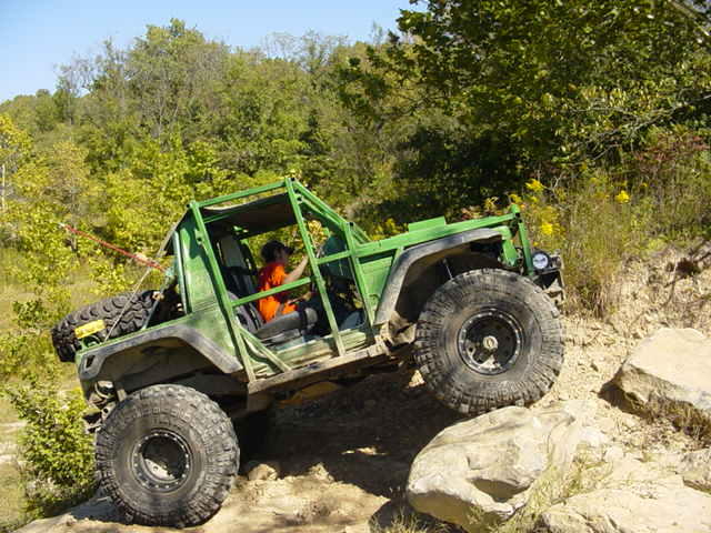 Green off-road vehicle with large tires climbing a rocky incline
