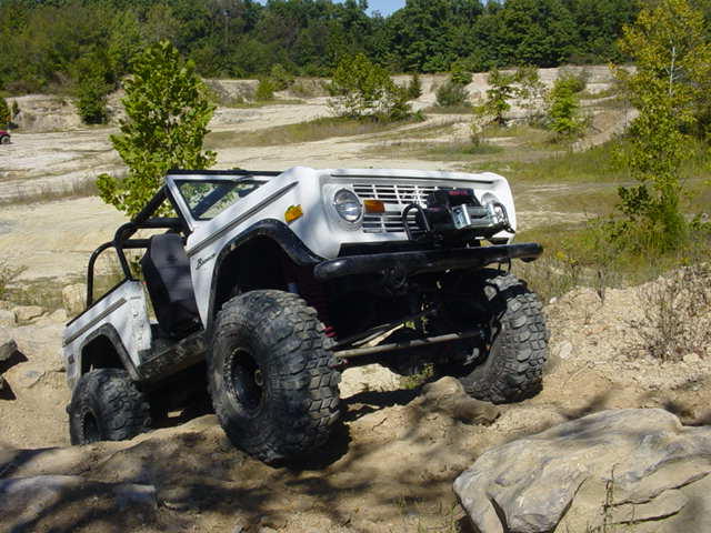 White Ford Bronco with large tires driving over rocks on a dirt trail