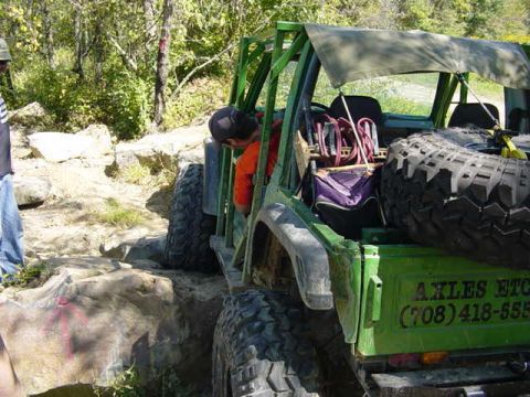 1992 Ford Bronco - A green off-road vehicle navigates a rocky terrain with a spare tire prominently displayed on its rear.