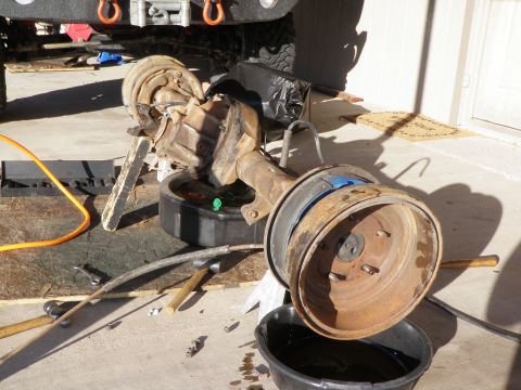 1982 Ford Bronco - A front axle assembly with drum brakes is shown resting on an oil drain pan, likely during a repair or maintenance procedure.