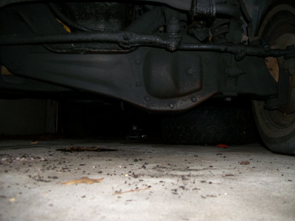 Underside view of a vehicle front differential, tie rod and tire over a concrete floor