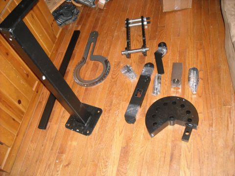 1979 Ford F-150 - Various parts for a pipe bender, including the main frame and several dies, are arranged on a wood floor.