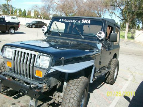1992 Jeep Wrangler - A black Jeep Wrangler is parked outside, showing its front grille and aftermarket fenders.