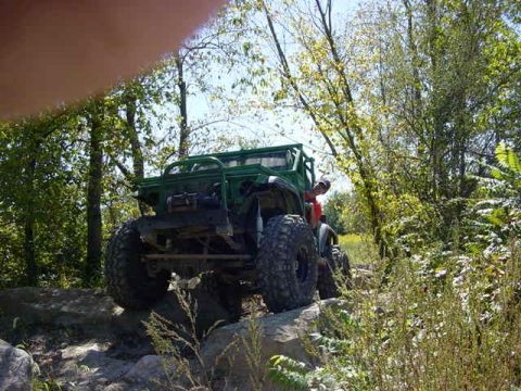1992 Ford Bronco - A modified off-road vehicle navigates a challenging rocky terrain surrounded by trees.