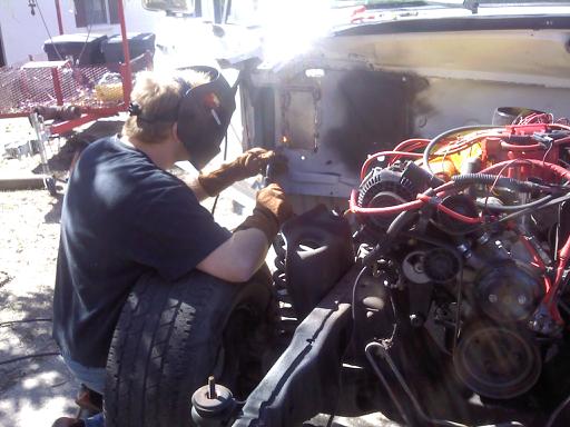Person in welding helmet welding on engine bay of stripped vehicle outdoors