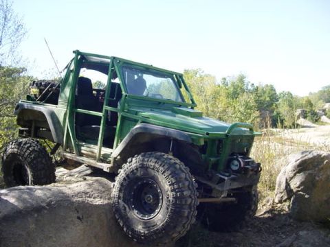 1992 Ford Bronco - A heavily modified green off-road vehicle navigates a rocky terrain under a clear sky.