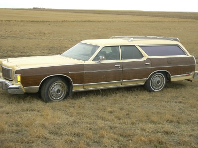 1978 Mercury Colony Park - This station wagon, likely a 1977 model, sits in a dry, grassy field under a cloudy sky.