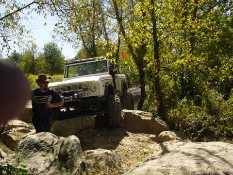 1992 Ford Bronco - A white off-road vehicle is shown on a , rocky path surrounded by trees.