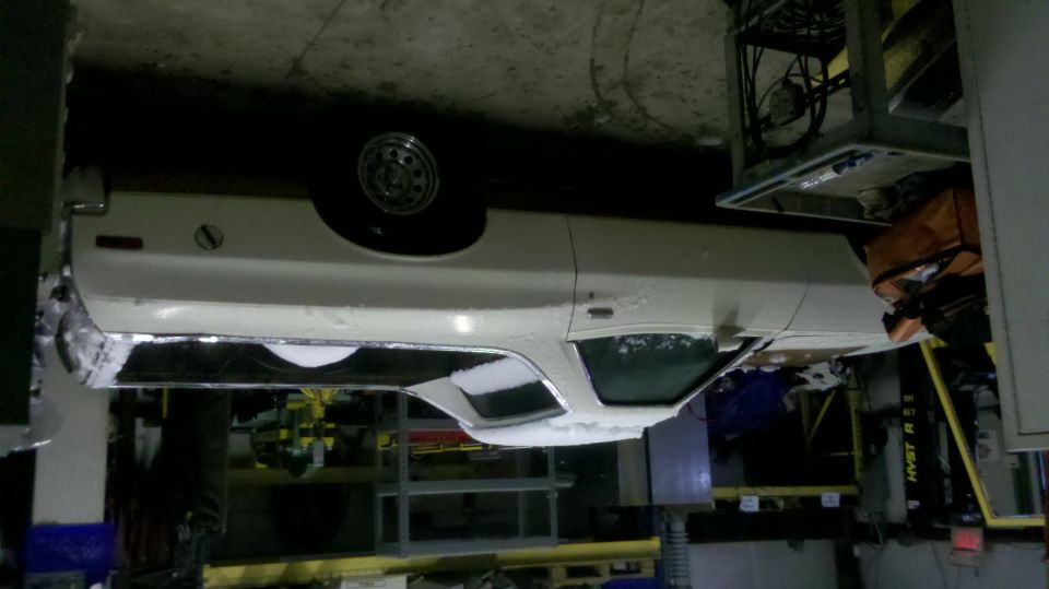 Upside-down rear view of a white Ranchero with spare tire in a garage shop