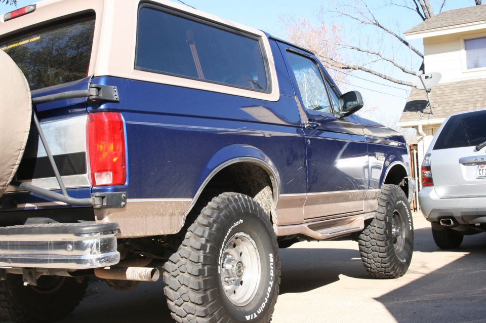 Lifted dark blue two-tone Ford Bronco with BFGoodrich Mud-Terrain tires, rear passenger-side view in a driveway
