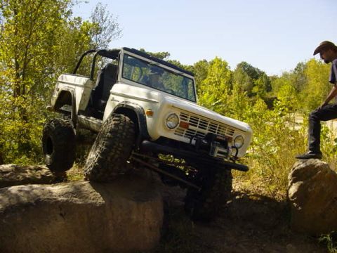 1992 Ford Bronco - A white 1970s Ford Bronco navigates a rocky trail with a person observing from a boulder.