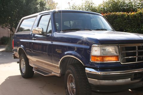 1996 Ford Bronco - A blue Ford Bronco is parked in a driveway with trees and bushes in the background.